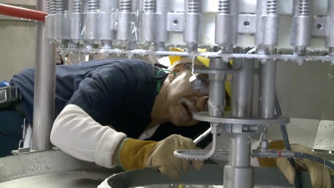 Imagen fija del video donde aparece un hombre con equipo de protección, sosteniendo una llave inglesa y mirando hacia la máquina.